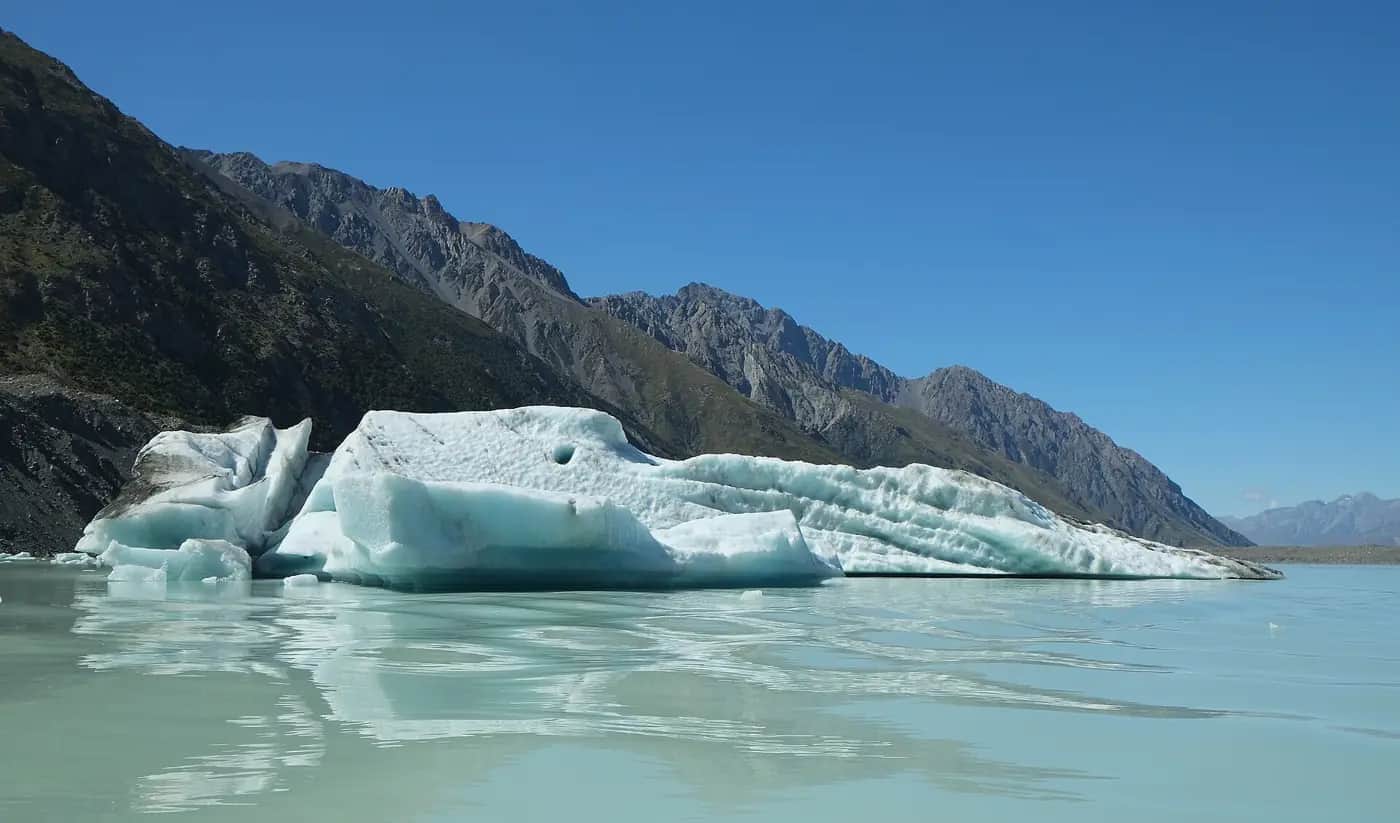 A blue iceberg floating in Tasman Glacier Lake below grey mountains