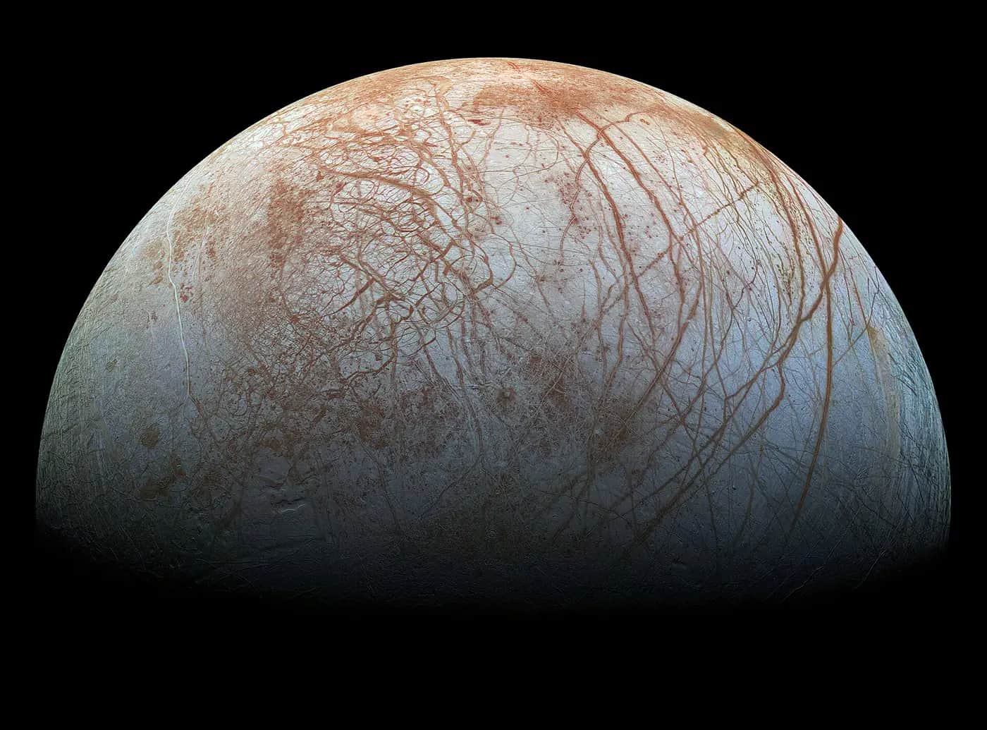 Jupiter's moon Europa, a pale icy sphere criss-crossed with reddish-brown cracks, against black space
