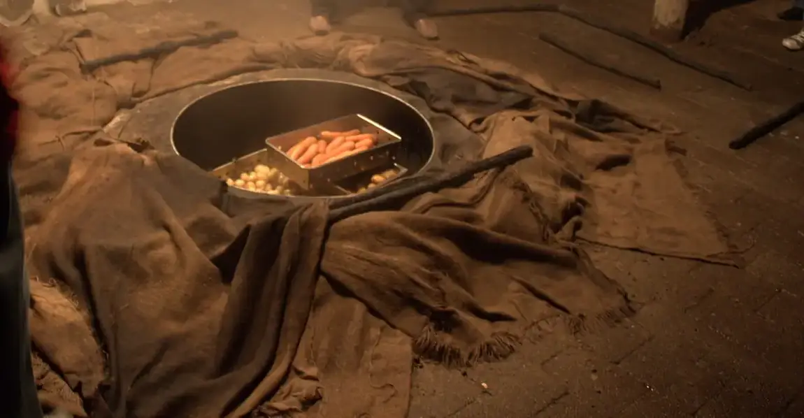 Steel baskets of potatoes and carrots in a round earth oven, surrounded by damp sacking, being uncovered at night