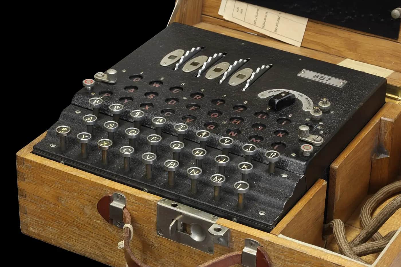 An Enigma cipher machine in its wooden case, with rows of round lettered keys, a panel of lamps and three rotor wheels