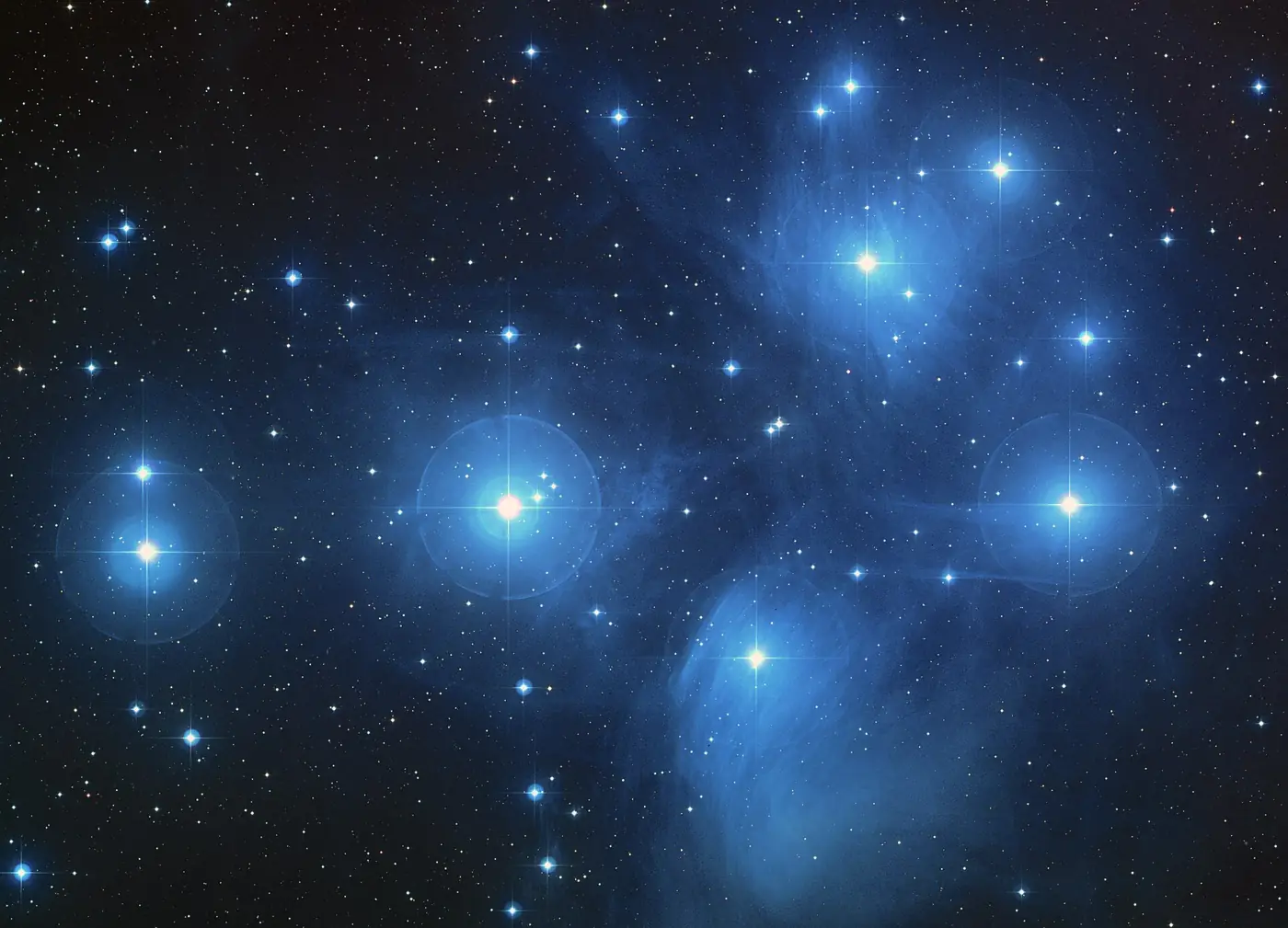 The Matariki star cluster: a group of bright blue-white stars wrapped in faint blue haze against a dark sky