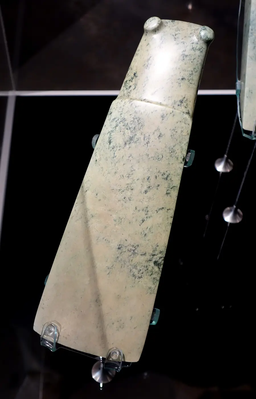 A long, smooth pale green toki pounamu (adze blade) displayed in a museum case