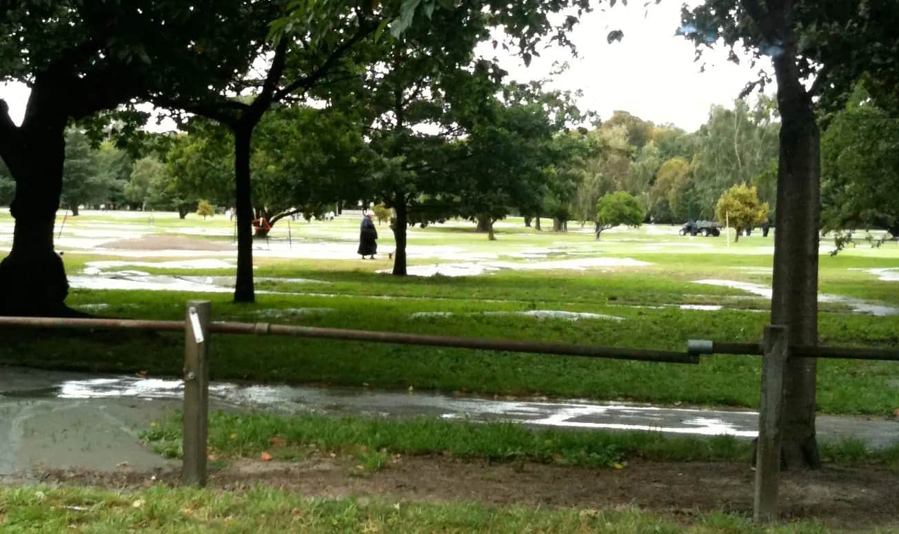 Grey silt and pools of water spread across the grass among trees in Hagley Park, Christchurch