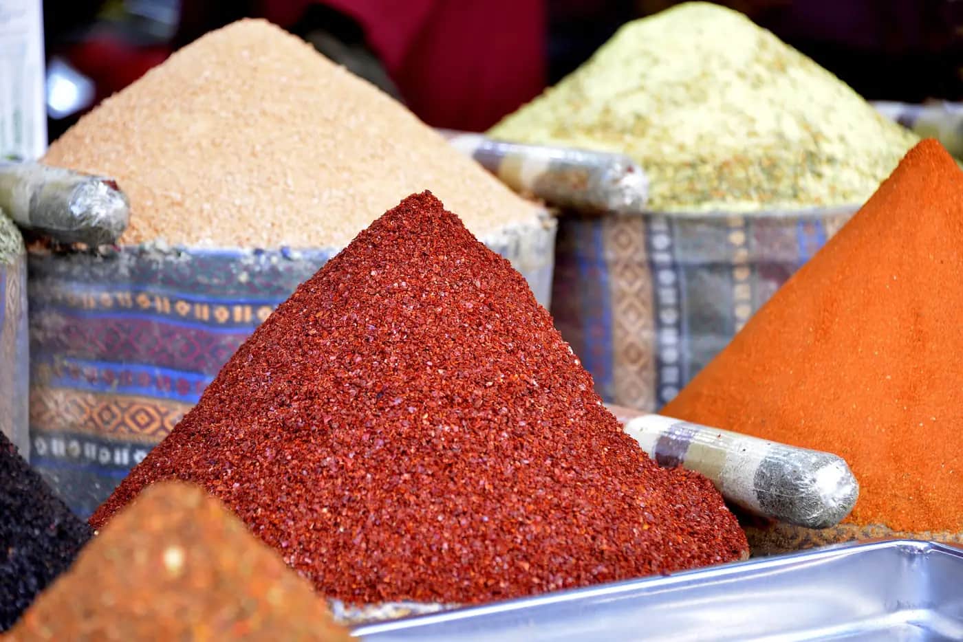 Tall cone-shaped heaps of red, orange, pale green and sandy-coloured ground spices at a market stall