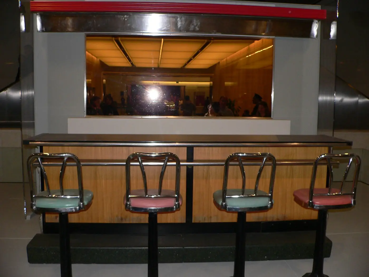 Four chrome stools with green and pink seats in front of a section of the original Woolworth's lunch counter on display in a museum