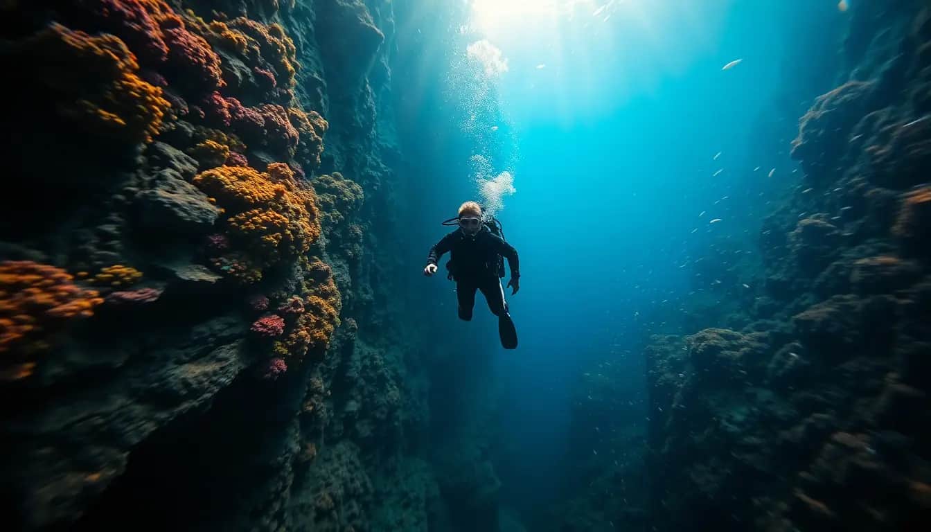 A scuba diver hovers beside a steep underwater cliff covered in orange and pink sponges, with sunlight shining down through deep blue water